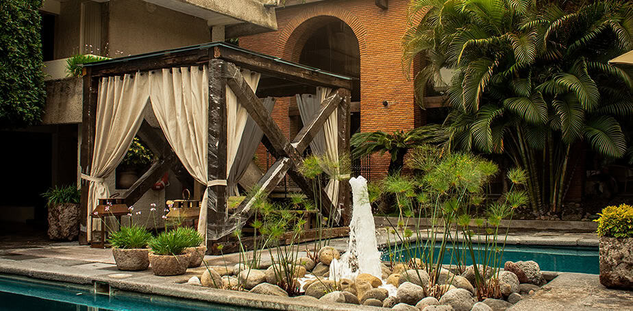 Zona de descanso con fuente y jard&iacute;n en hotel en Le&oacute;n, M&eacute;xico, rodeada de vegetaci&oacute;n tropical y ambiente relajante.