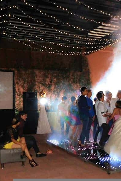 Boda en salón decorado con luces y música en vivo, con invitados disfrutando de la celebración en un ambiente elegante y fest.