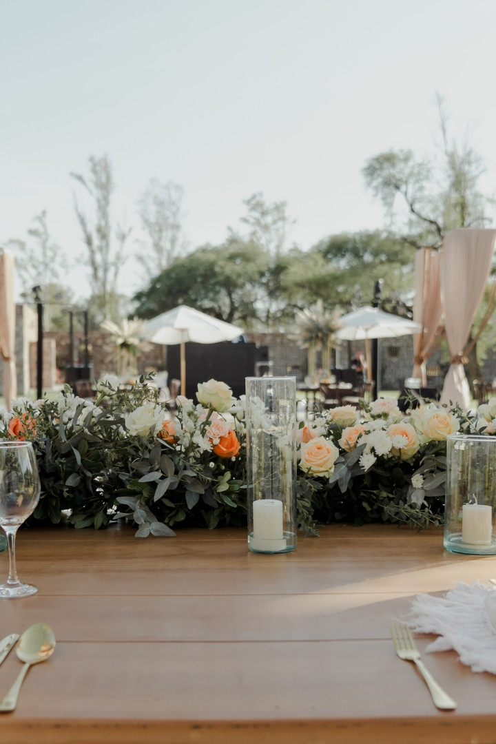 Mesa decorada con flores, velas y cristalería en un evento al aire libre.