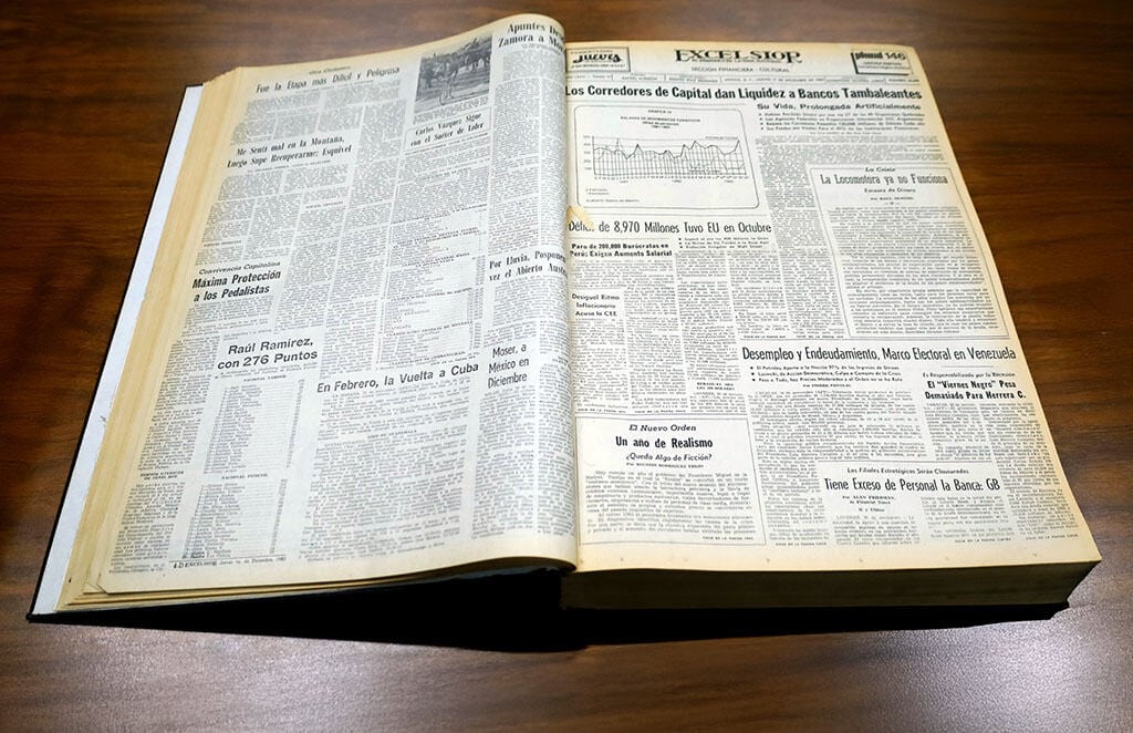 Libro abierto con peri&oacute;dicos en una mesa, detalles de noticias financieras y econ&oacute;micas, lectura informativa y actualizada.