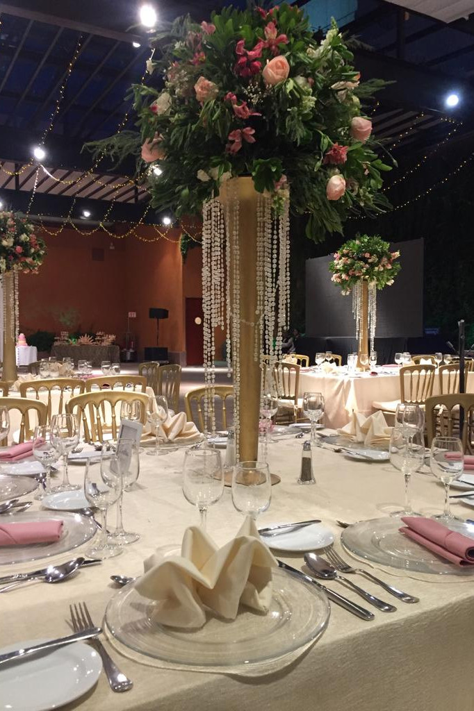 Mesa decorada con flores y cristalería en un salón de eventos sofisticado.