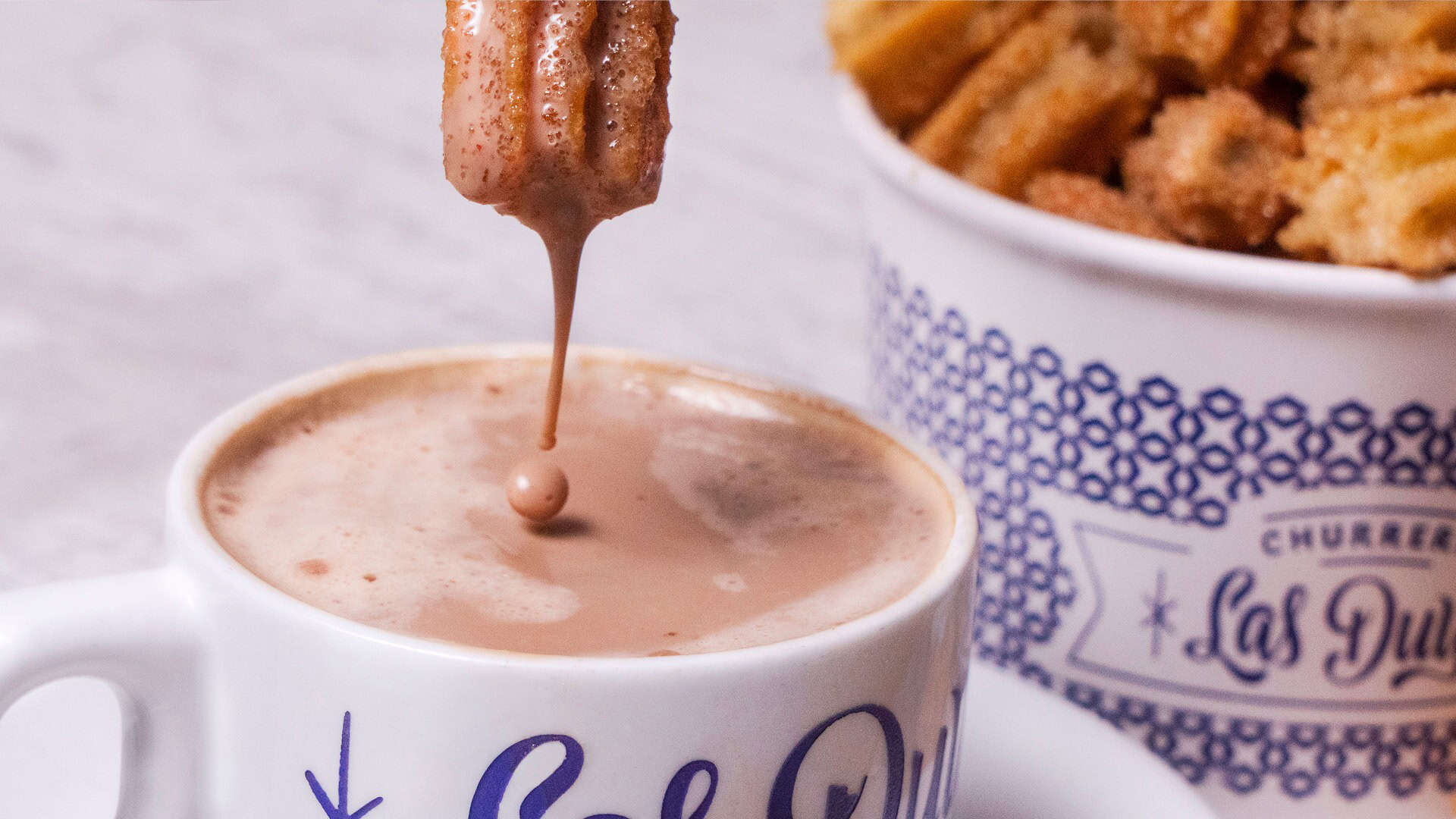 Taza de chocolate caliente con churros crujientes y espolvoreados con az&uacute;car, perfecta para disfrutar en Le&oacute;n, M&eacute;xico.