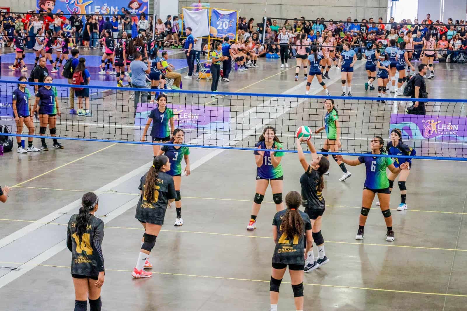 Jugadoras de voleibol en acción durante torneo escolar en León, Guanajuato, con público y equipos en competencia.