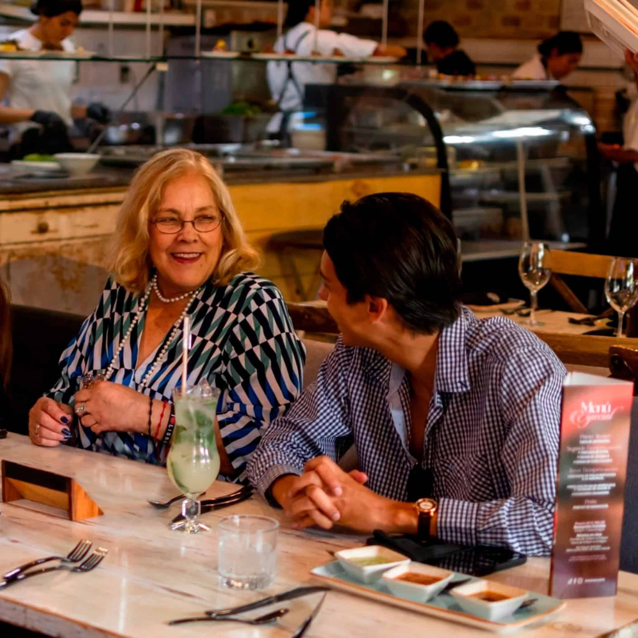 Mujer y hombre conversando y riendo en un restaurante sofisticado en León, con ambiente acogedor y servicio de calidad.