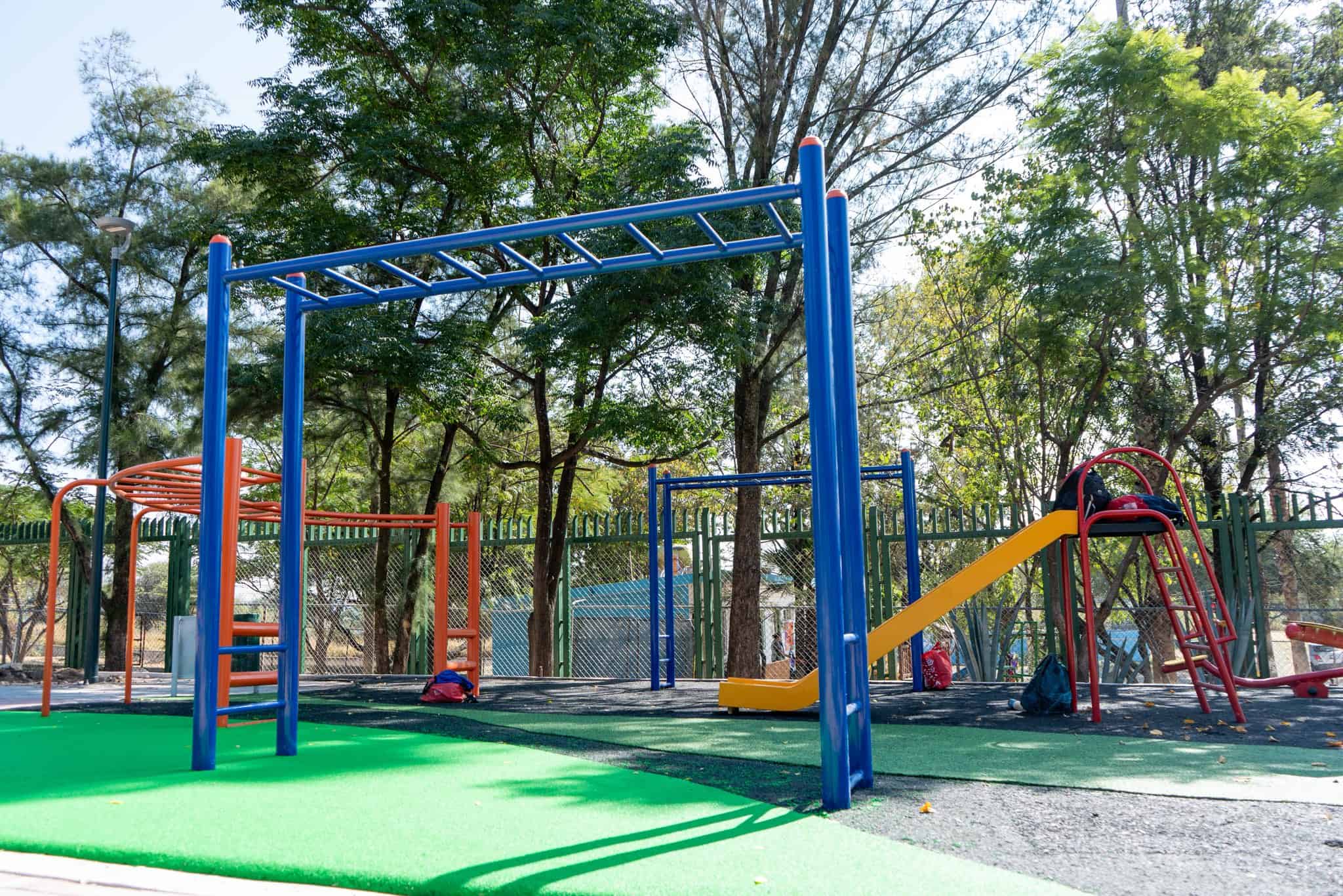 Juegos infantiles en parque p&uacute;blico con columpios, resbaladillas y estructuras de juego en un espacio al aire libre rodeado d.