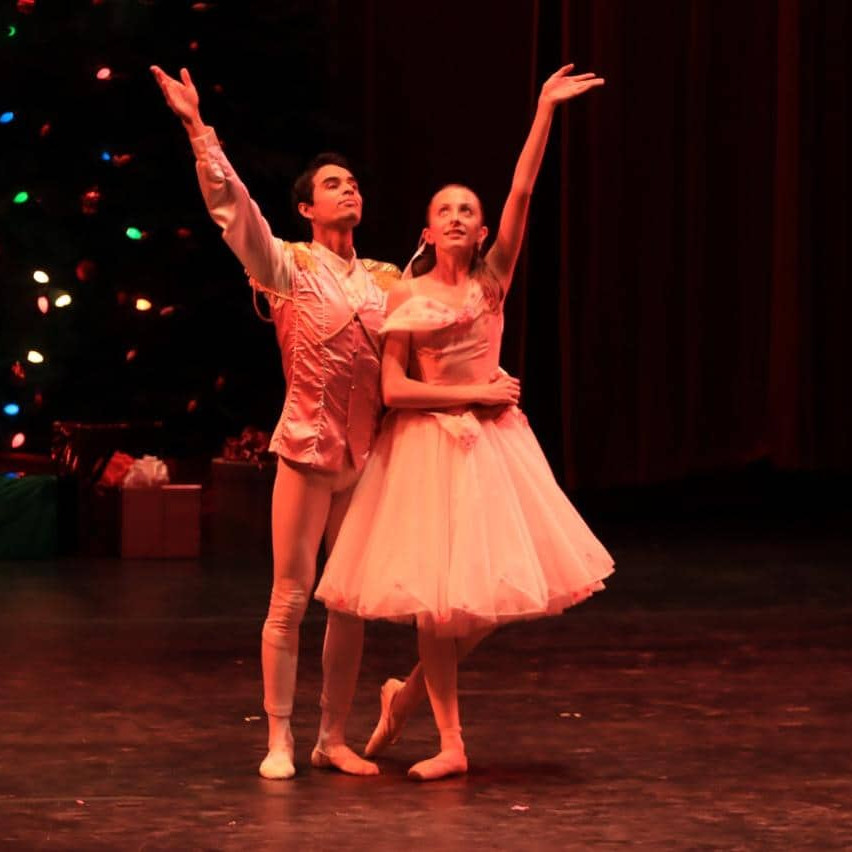 Bailarines en escenario con fondo de árbol de Navidad iluminado, representando una actuación artística y cultural en León, Mé.