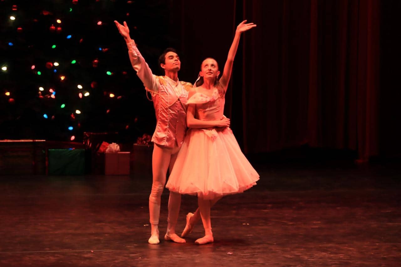Bailarines en escenario con fondo de árbol de Navidad iluminado, representando una actuación artística y cultural en León, Mé.