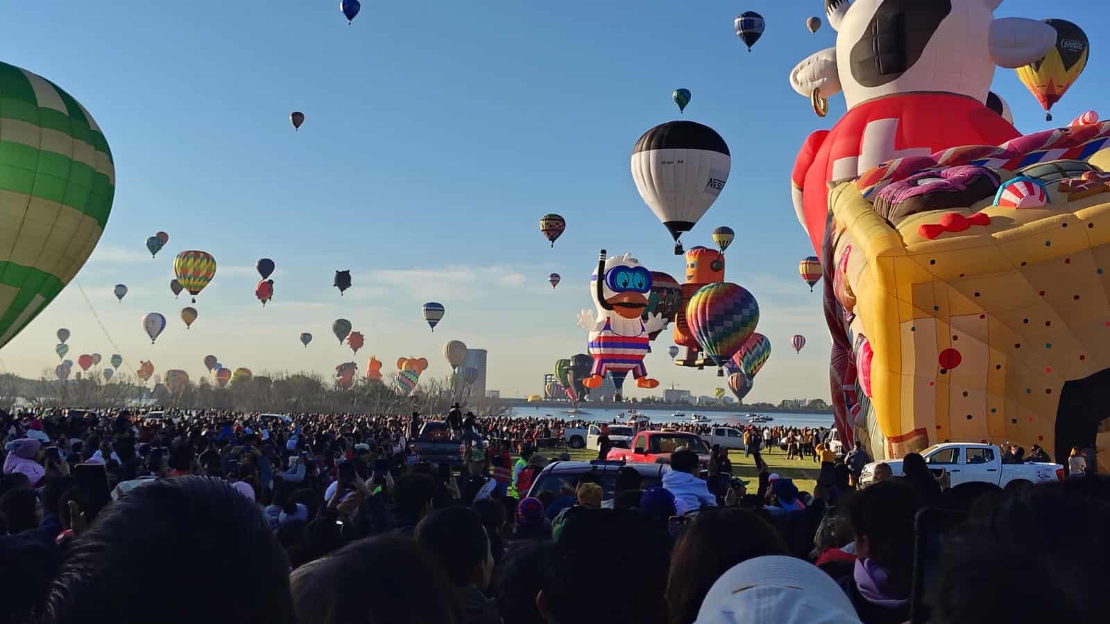 Espectáculo de globos aerostáticos en León, México, con numerosos globos de colores y formas en un evento al aire libre.