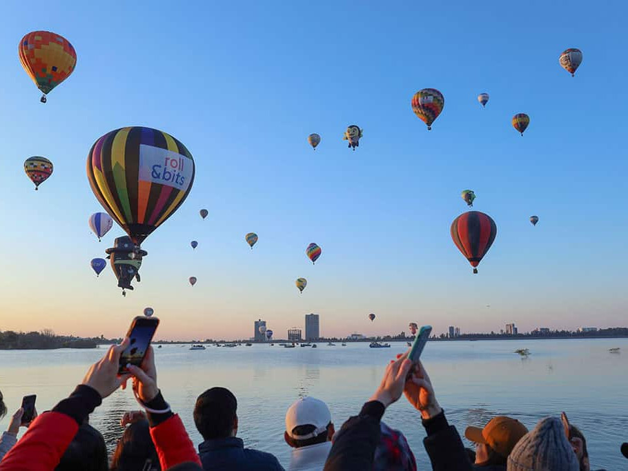Espectáculo de globos aerostáticos en León, México, con numerosos globos coloridos en el cielo al amanecer sobre el río.