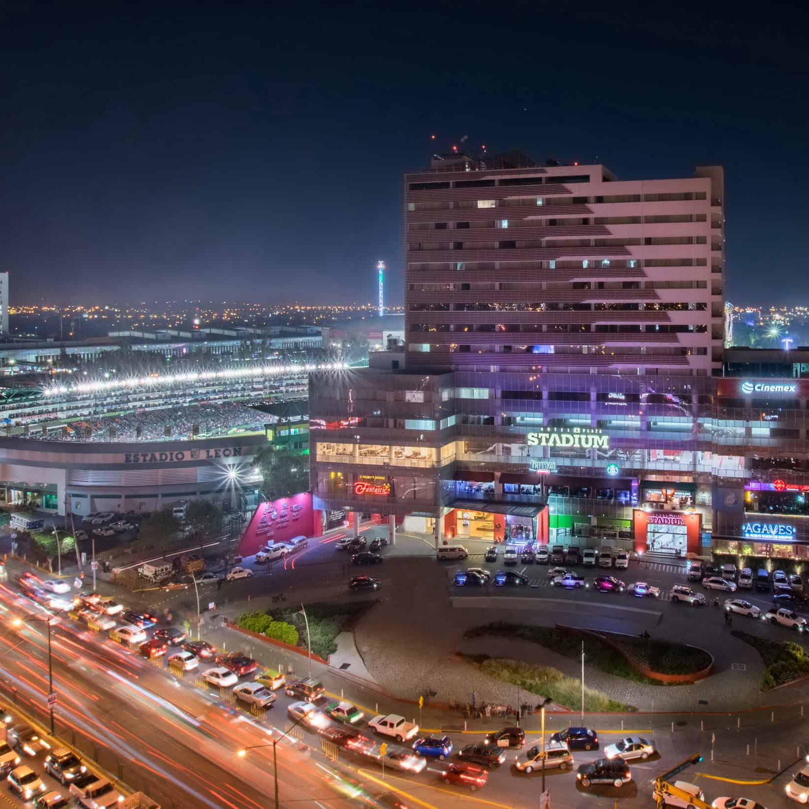 Vista panorámica del centro de León, con el estadio y calles llenas de vida y luces en la noche.