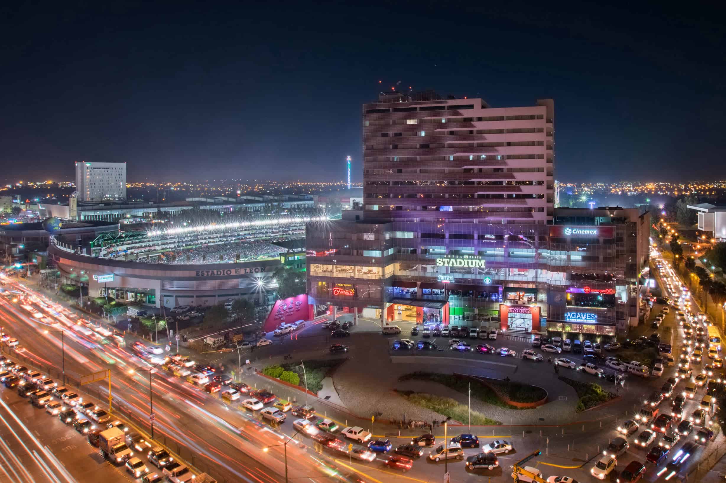 Vista panorámica del centro de León, con el estadio y calles llenas de vida y luces en la noche.