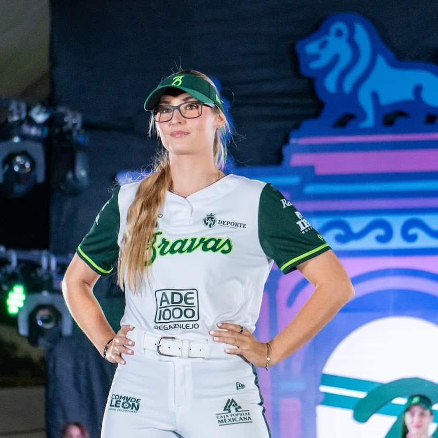 Mujer con camiseta de béisbol en escenario, diseño de león y logotipos deportivos, en evento cultural en León, México.