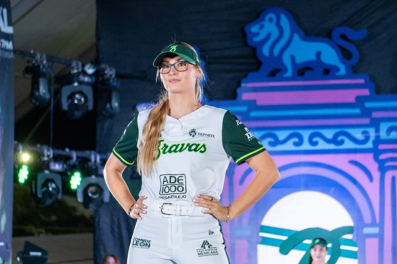Mujer con camiseta de béisbol en escenario, diseño de león y logotipos deportivos, en evento cultural en León, México.