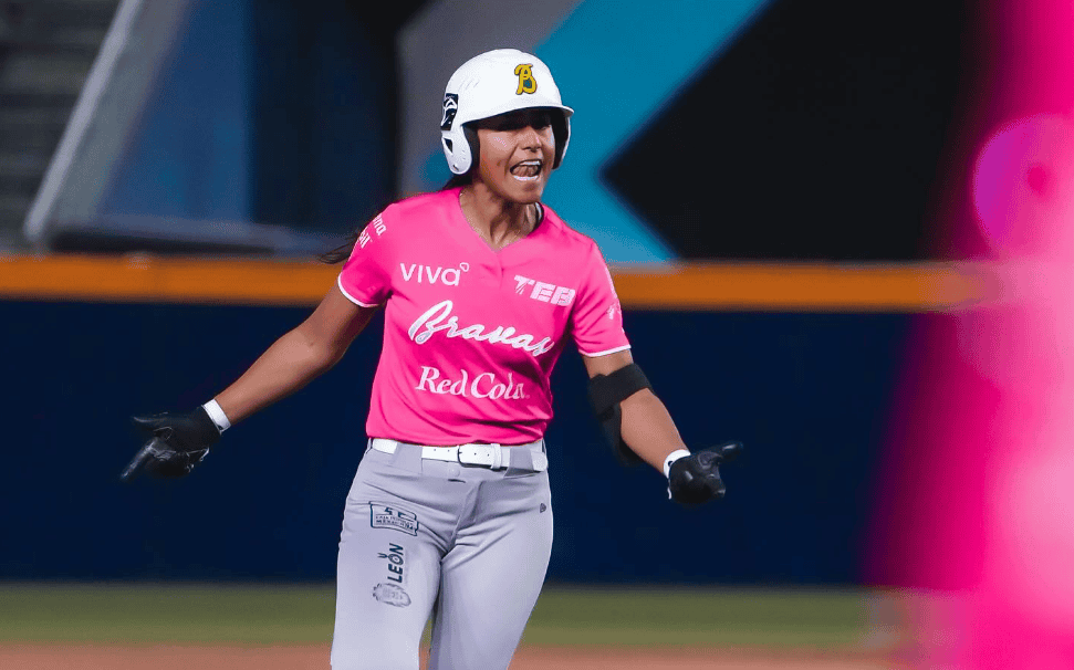 Deportista femenina celebrando en un juego de b&eacute;isbol con uniforme rosa y casco.