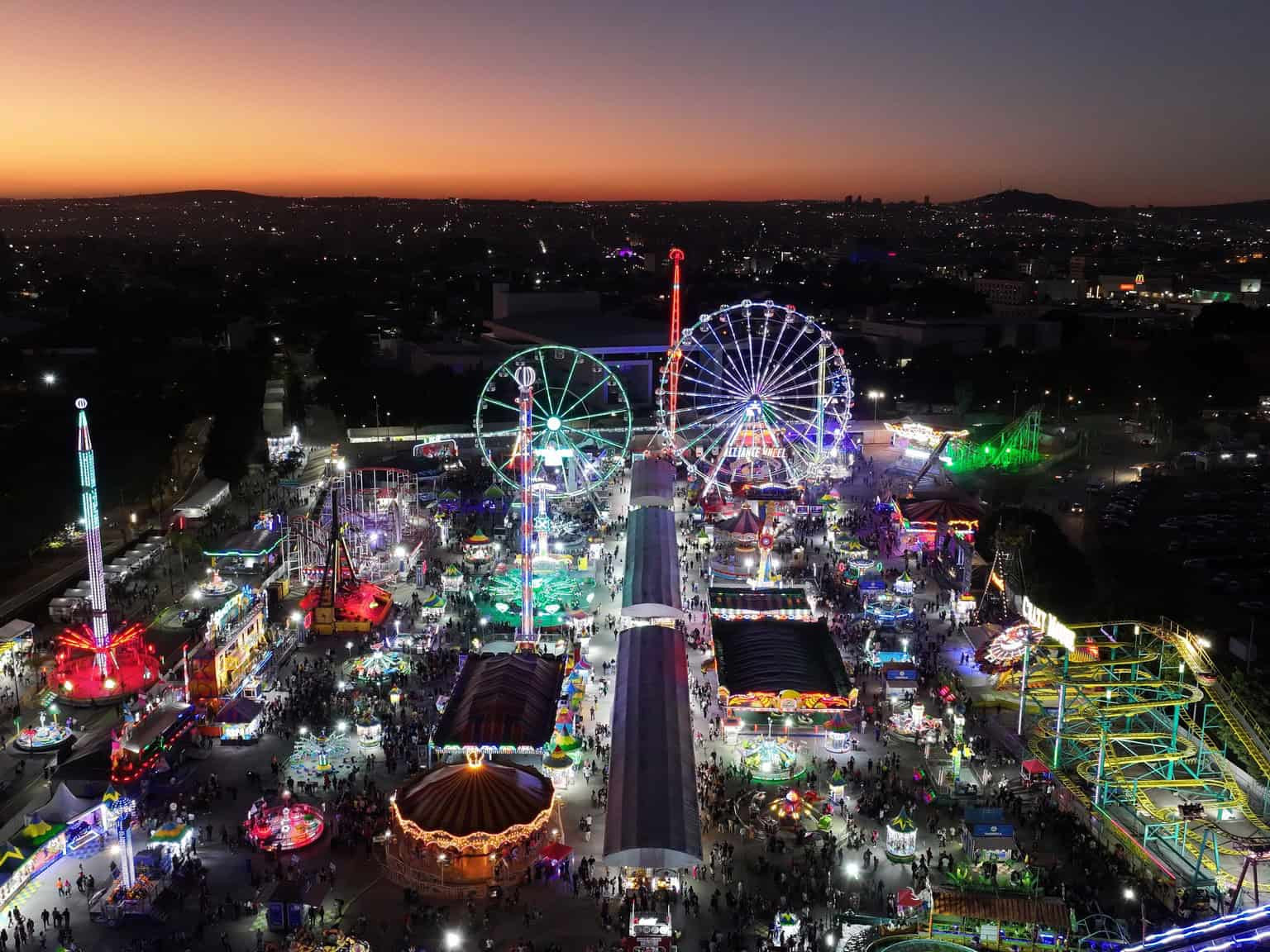 Feria nocturna en León, México con noria gigante, juegos mecánicos y luces vibrantes, ideal para diversión familiar y turista.