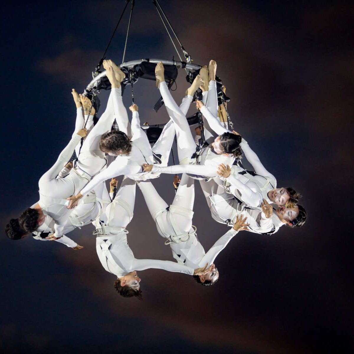Espectáculo de circo aéreo con artistas en trajes blancos realizando acrobacias en el aire.