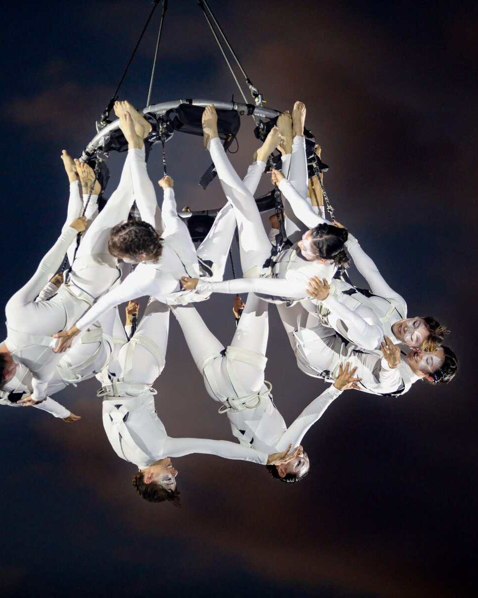 Espectáculo de circo aéreo con artistas en trajes blancos realizando acrobacias en el aire.