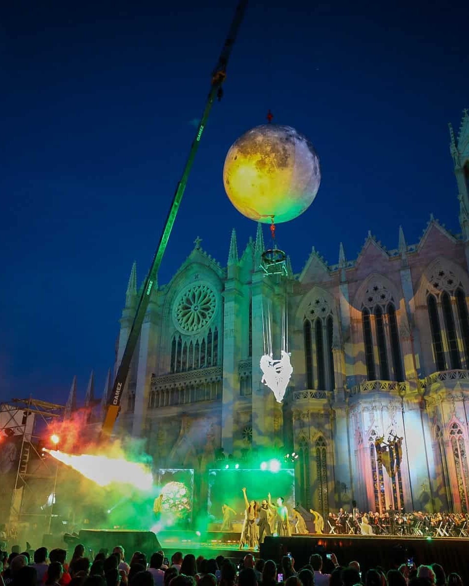 Espectáculo nocturno en la Catedral de León con luces, música y un globo gigante en el cielo, creando un ambiente mágico y fe.