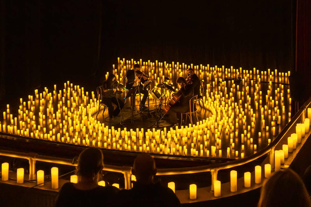 Cuatro m&uacute;sicos tocando en un escenario rodeado de velas en un ambiente &iacute;ntimo y c&aacute;lido.