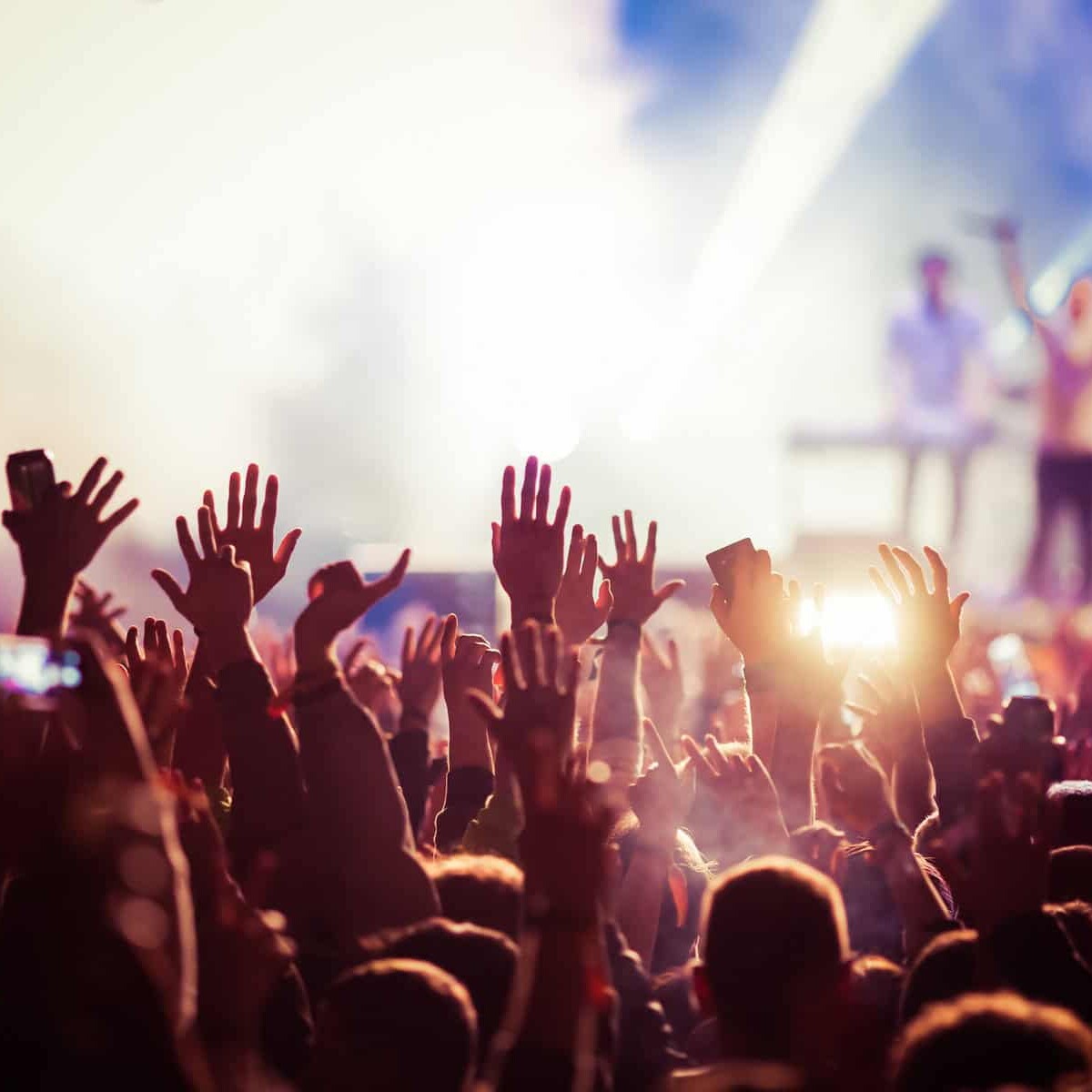 Multitud disfrutando de un concierto en vivo con luces brillantes y artistas en el escenario.