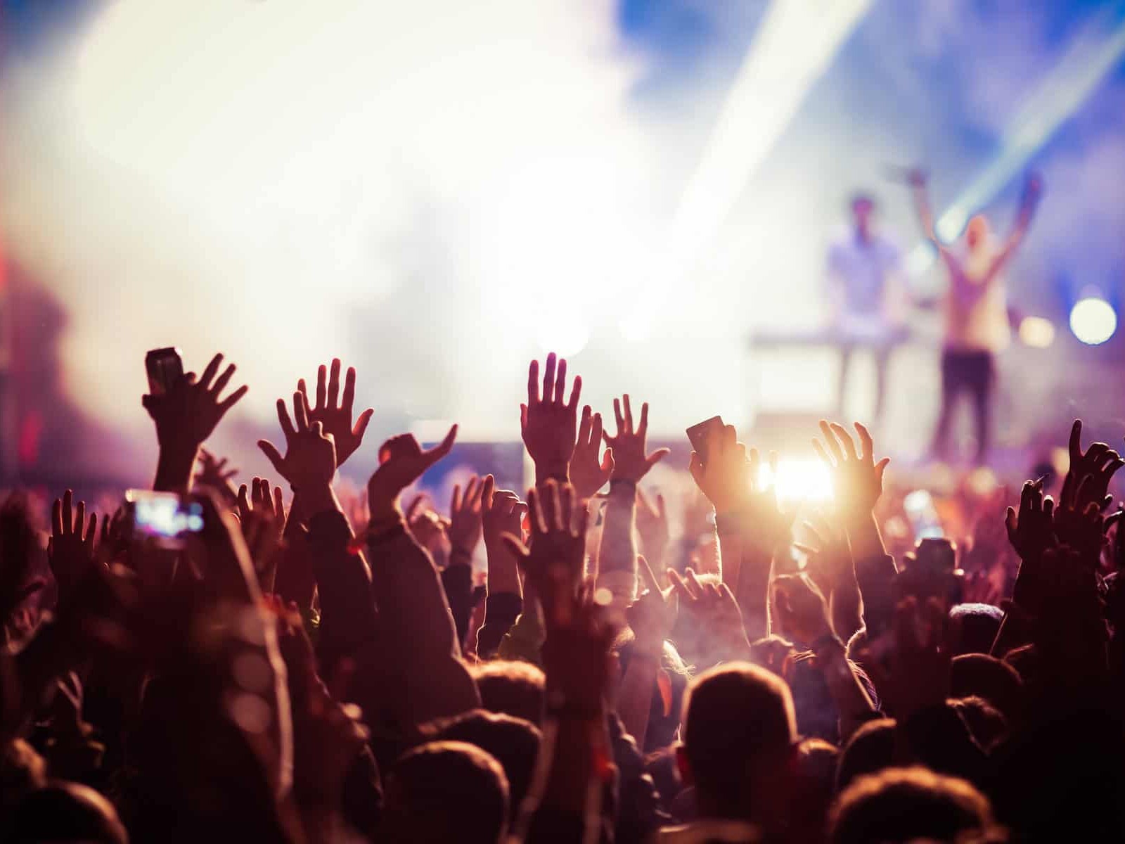 Multitud disfrutando de un concierto en vivo con luces brillantes y artistas en el escenario.