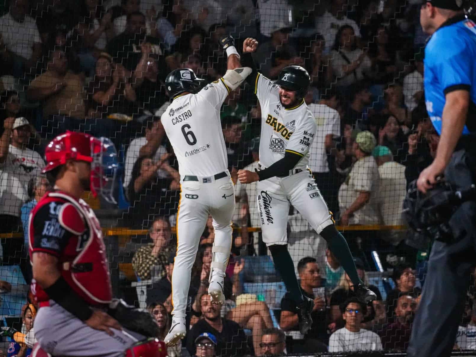Jugadores celebran una victoria en un partido de béisbol con público en las gradas.