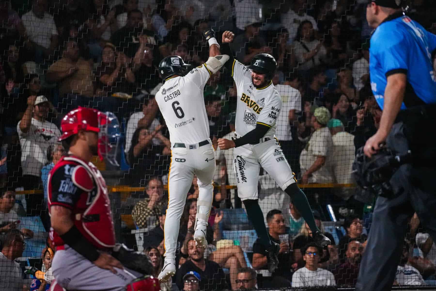 Jugadores celebran una victoria en un partido de béisbol con público en las gradas.