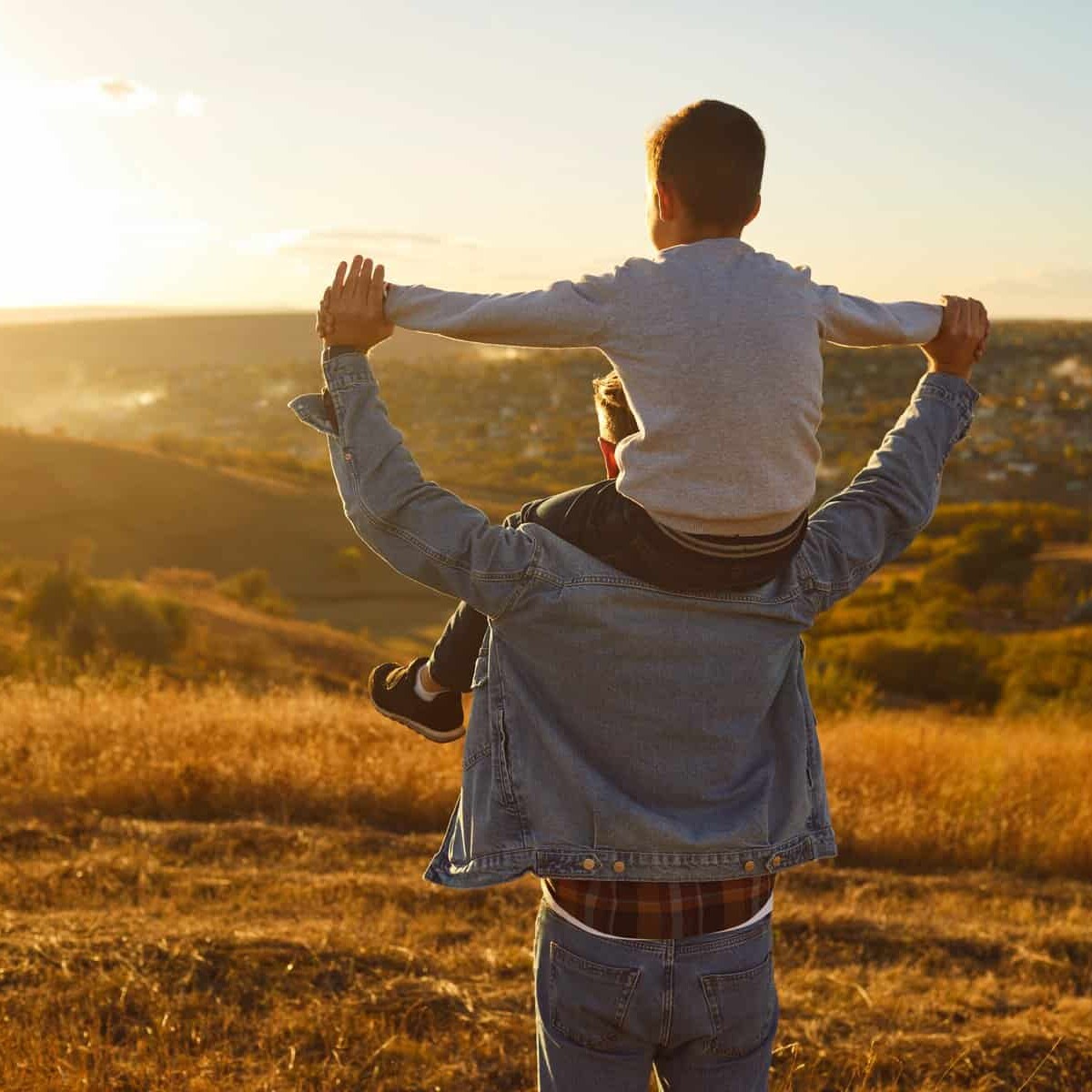 Paisaje de campo con un adulto y un niño disfrutando del atardecer, capturando momentos de felicidad y conexión en un entorno.