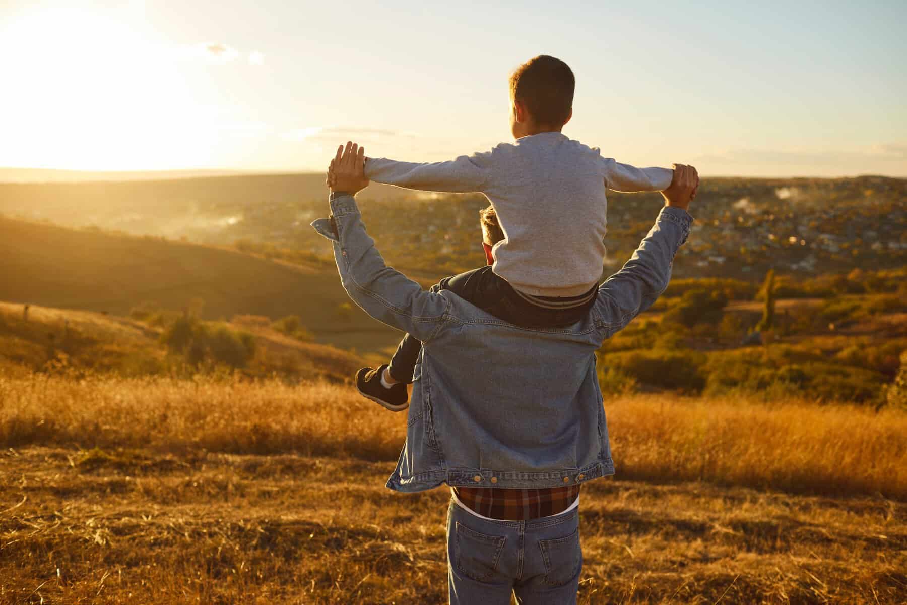 Paisaje de campo con un adulto y un niño disfrutando del atardecer, capturando momentos de felicidad y conexión en un entorno.