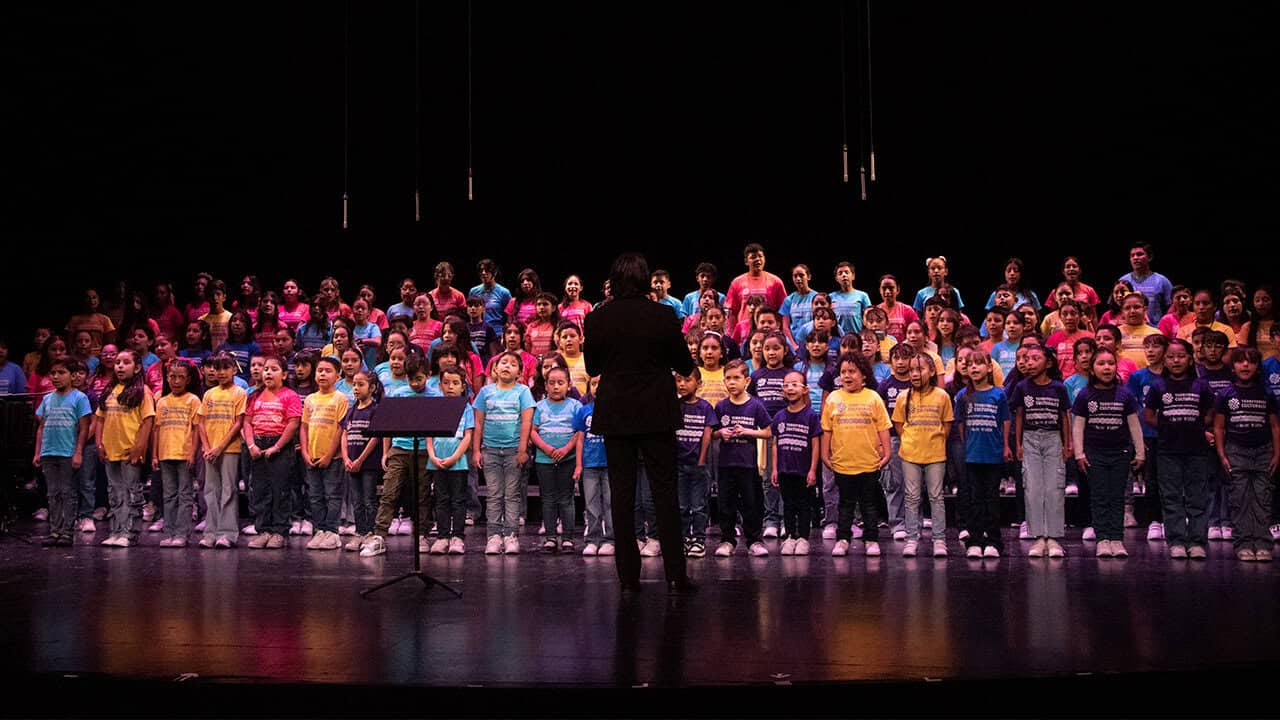 Coral infantil en concierto en el escenario de Le&oacute;n, M&eacute;xico, con ni&ntilde;os cantando y un director en el centro.