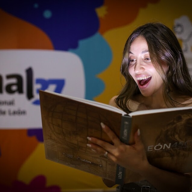 Excited woman reading at the book fair in León, with the event “León 450: Leaving a Mark on History” in the background.
