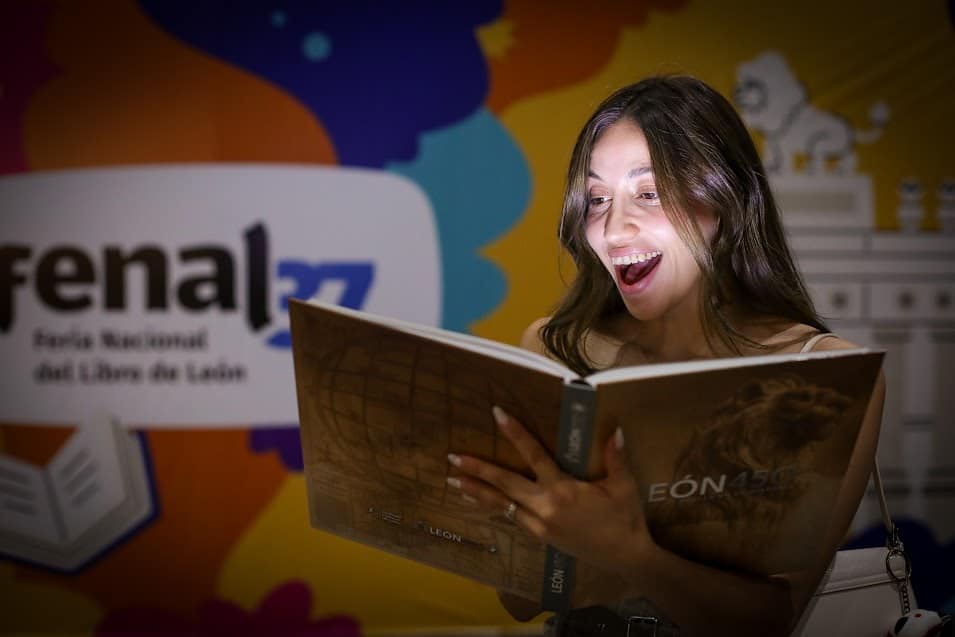 Excited woman reading at the book fair in León, with the event “León 450: Leaving a Mark on History” in the background.