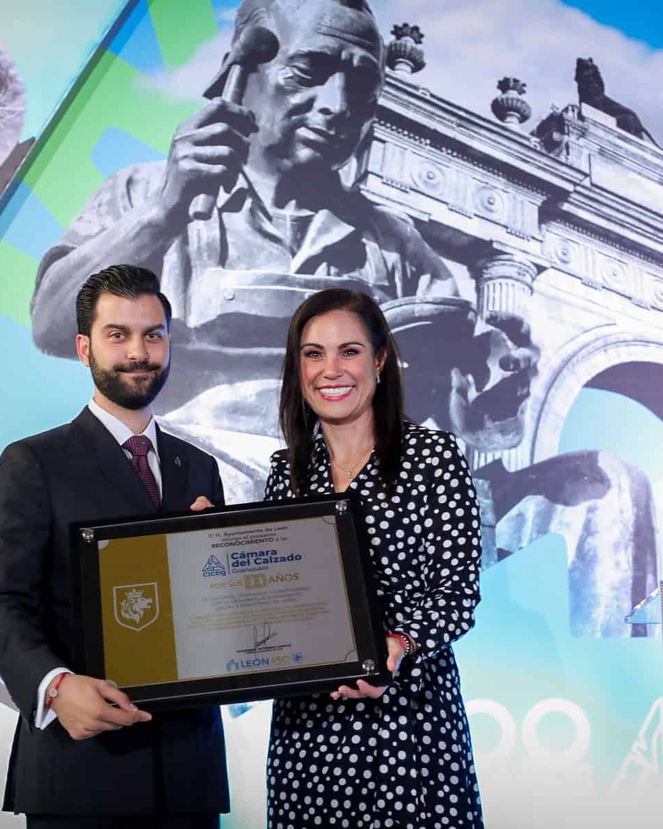 Dos personas en ceremonia de premiación en León, con monumentos históricos y arte en el fondo, celebrando logros culturales y.