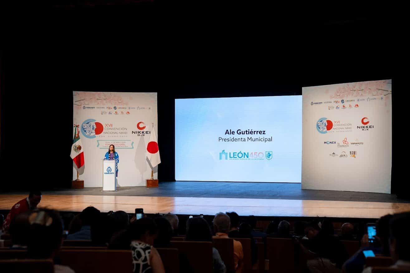 Alcaldesa Ale Gutiérrez en evento oficial en León, México, en un escenario con pantallas y banderas.