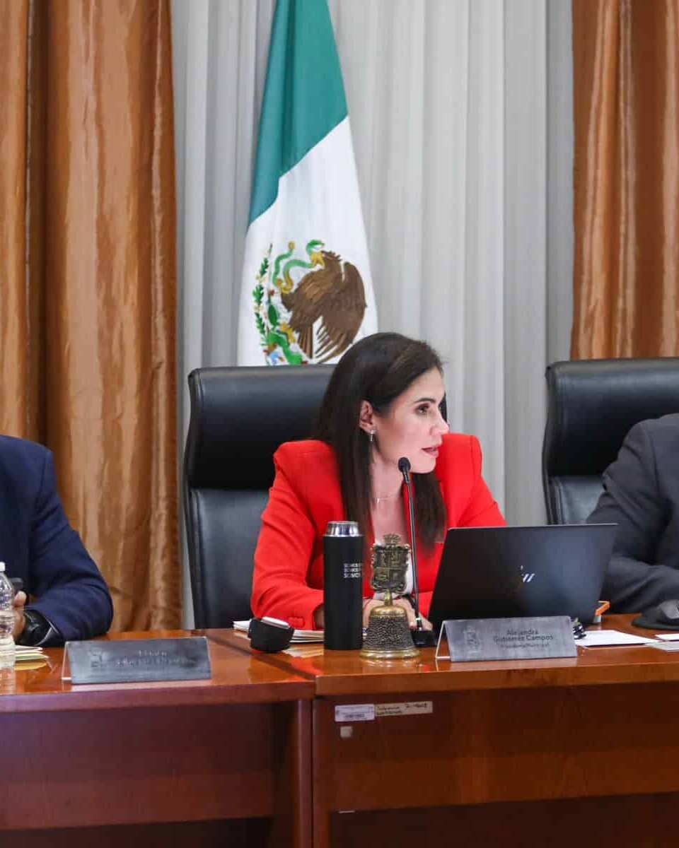 Tres funcionarios en una reunión oficial en el Palacio de Gobierno de León, con la bandera de México al fondo.