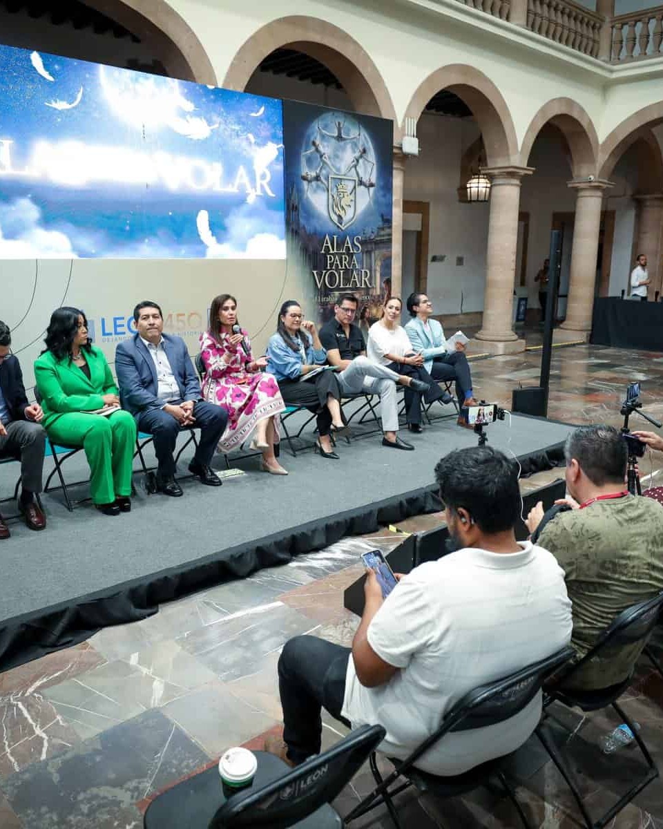 Panel de expertos en un evento en León, México, con audiencia y pantalla grande en un espacio histórico y elegante.