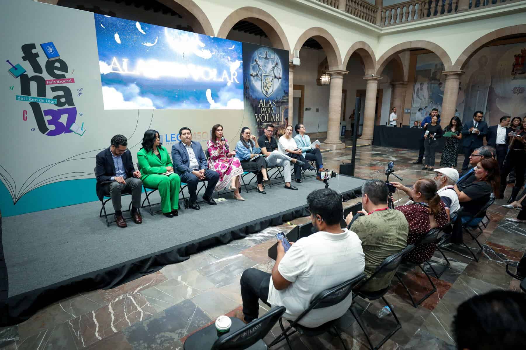 Panel de expertos en un evento en León, México, con audiencia y pantalla grande en un espacio histórico y elegante.
