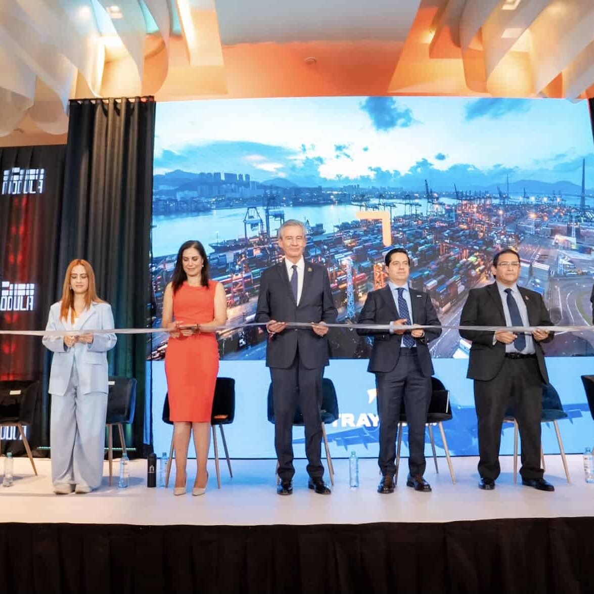 Grupo de personas en un escenario durante una inauguración con pantalla grande de fondo en León, Guanajuato, México.