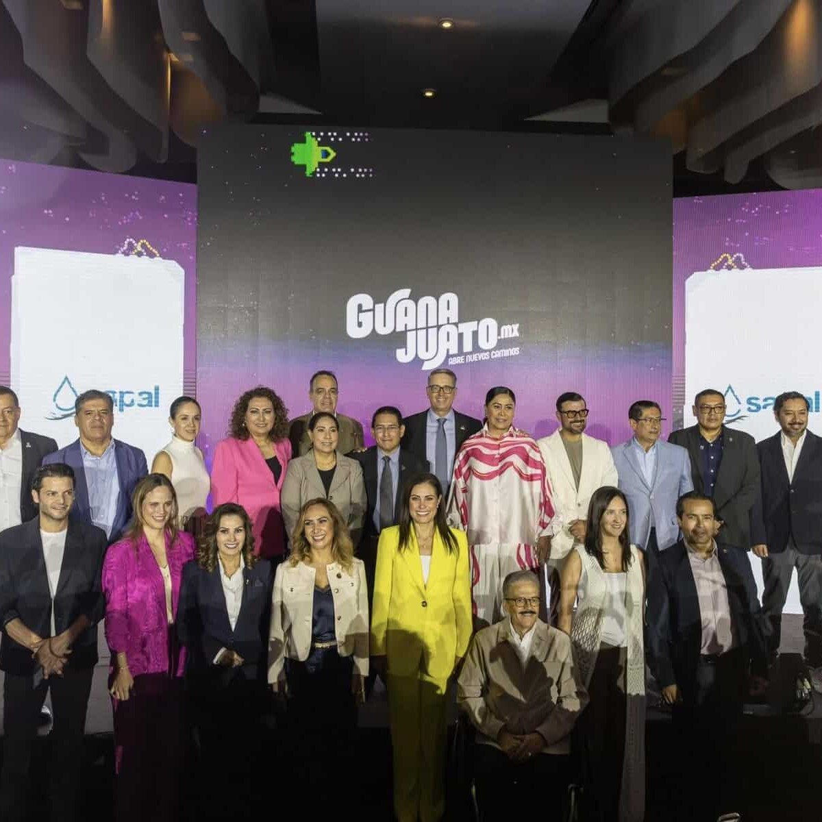 Grupo de personas en un evento cultural en León, Guanajuato, con escenario y pantallas grandes de fondo.