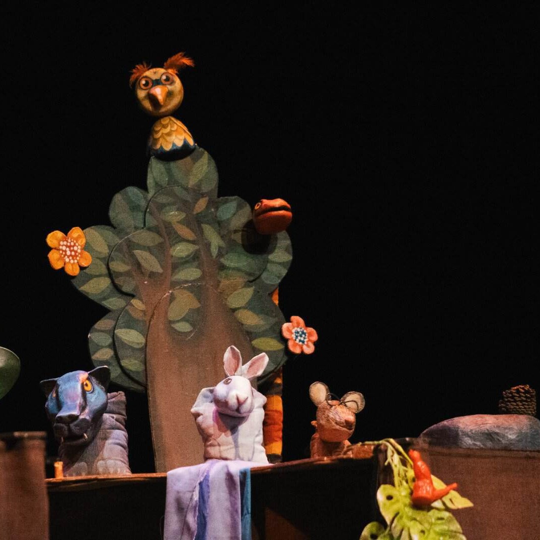 Árbol de títeres con personajes de marionetas en escenario oscuro, incluyendo un búho, una oveja, un ratón y una rana, en una.