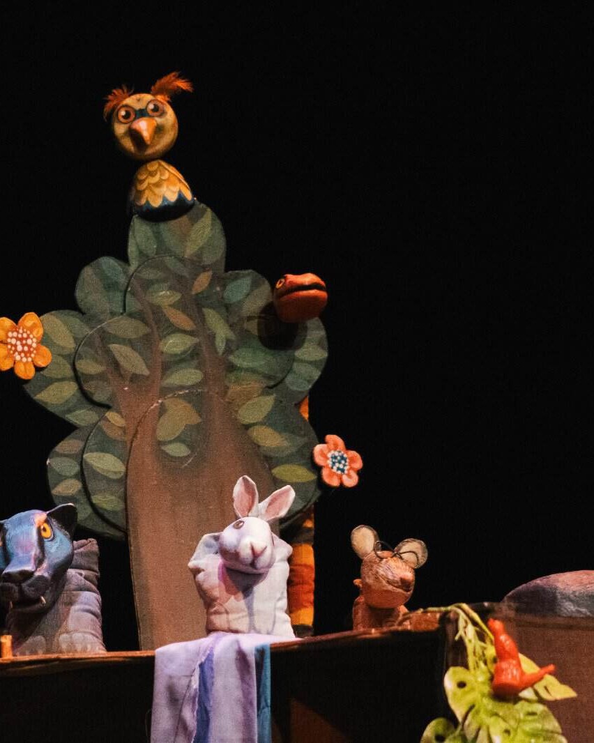Árbol de títeres con personajes de marionetas en escenario oscuro, incluyendo un búho, una oveja, un ratón y una rana, en una.