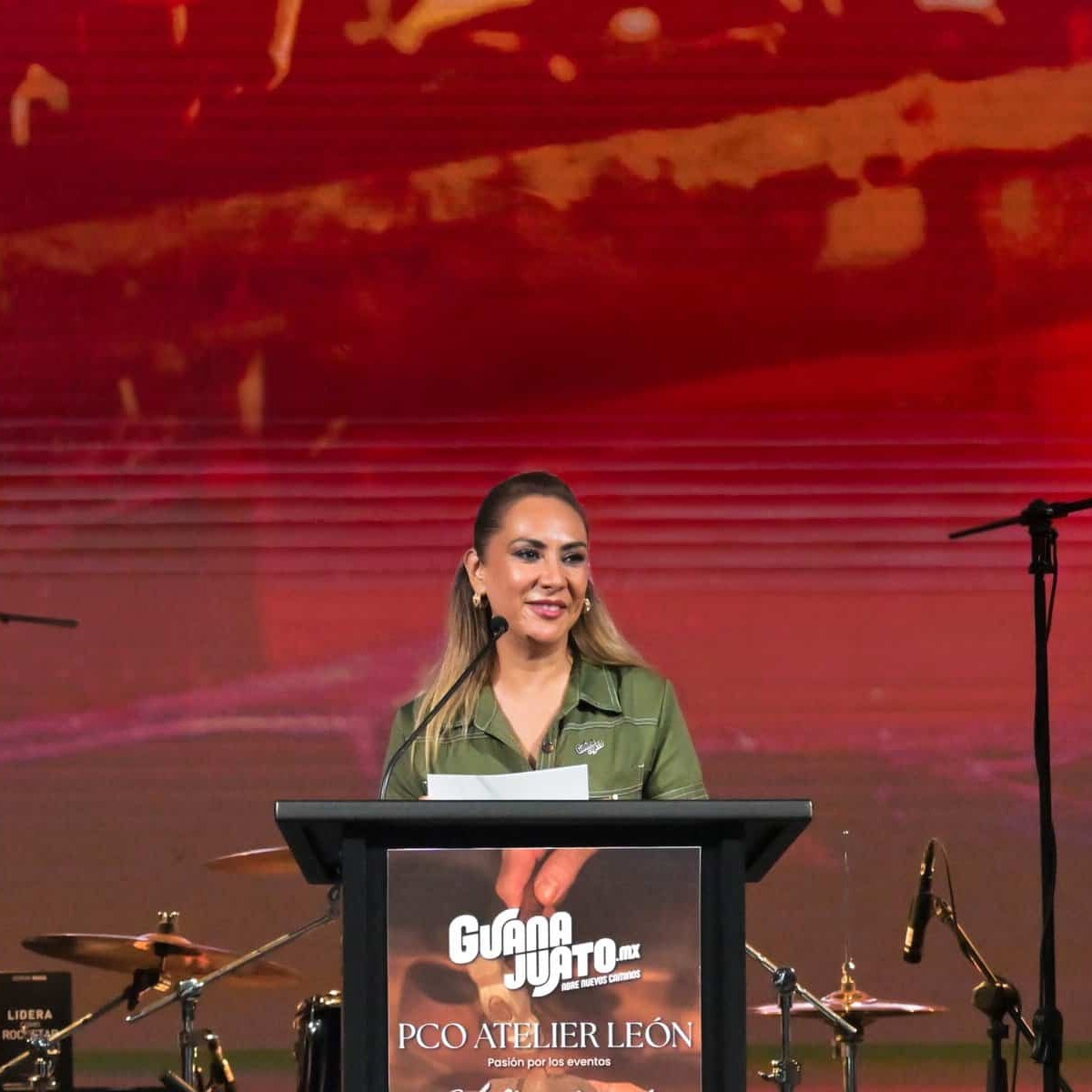 Mujer en escenario durante PCO Atelier 2026 en León, Guanajuato, México, con fondo rojo y micrófonos.