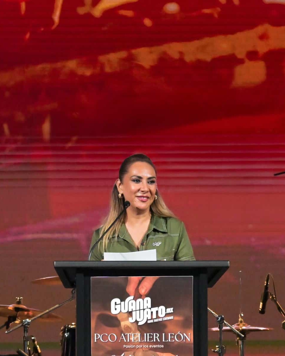 Mujer en escenario durante PCO Atelier 2026 en León, Guanajuato, México, con fondo rojo y micrófonos.