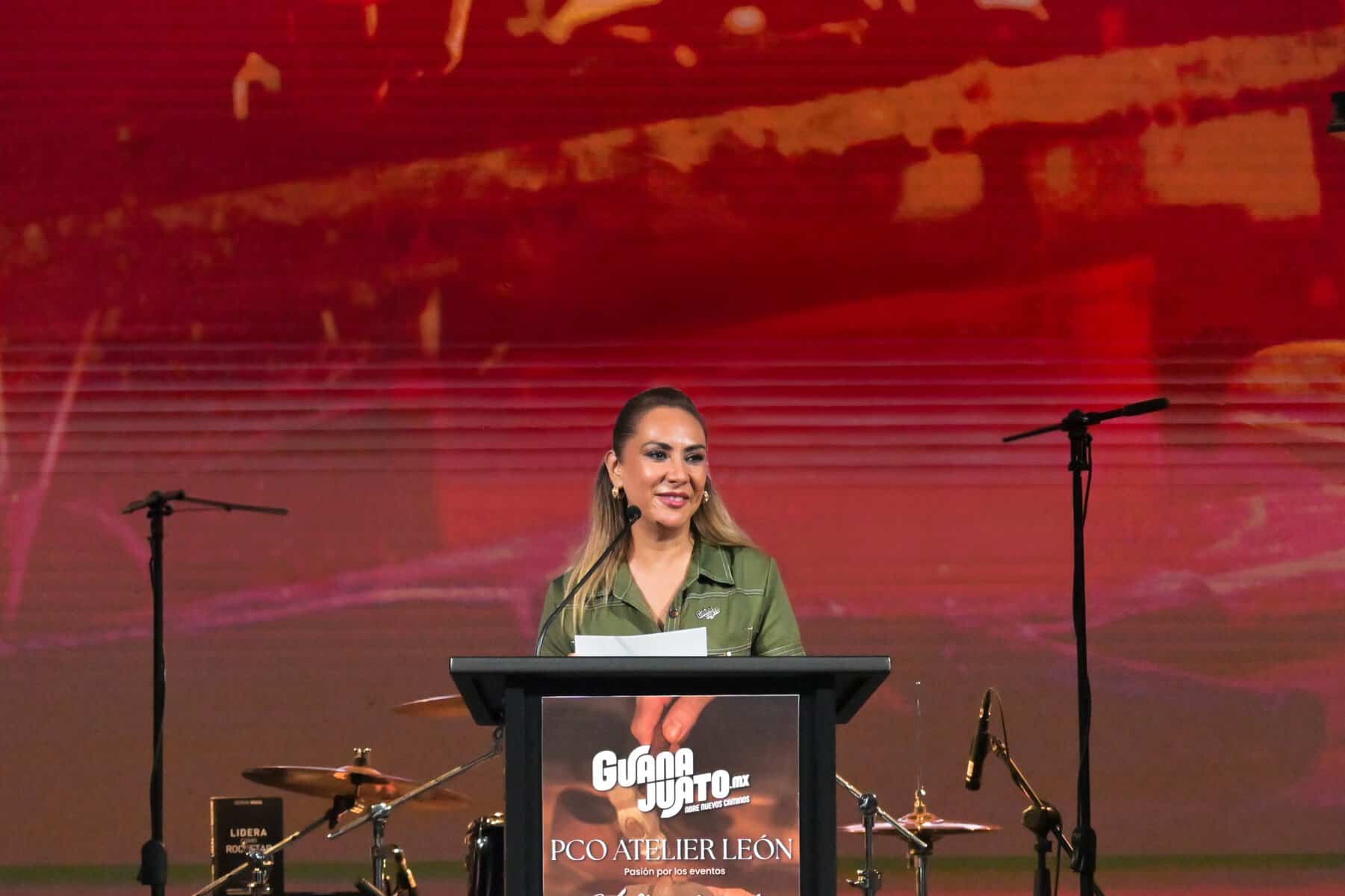 Mujer en escenario durante PCO Atelier 2026 en León, Guanajuato, México, con fondo rojo y micrófonos.