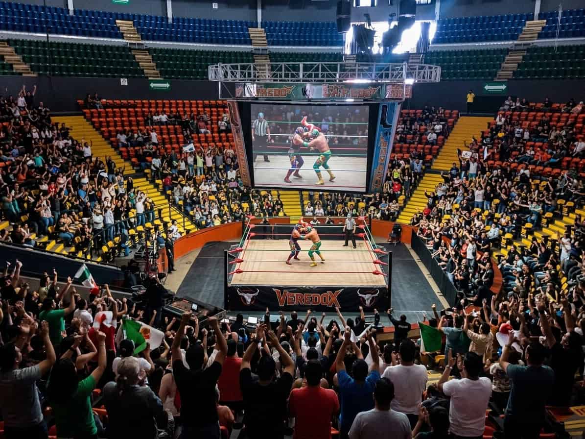 Lucha libre en León, México, con luchadores en el ring y público animado en un evento deportivo.