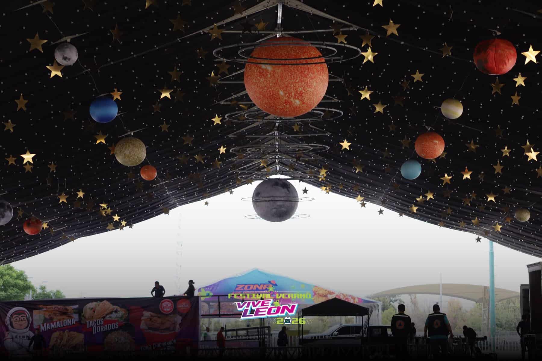 Decoración temática espacial en Vive León 2026, con planetas y estrellas colgantes en el festival de verano.