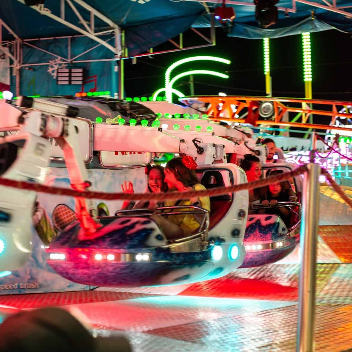 Atracción de feria en León con luces de neón y niños disfrutando en las naves espaciales.