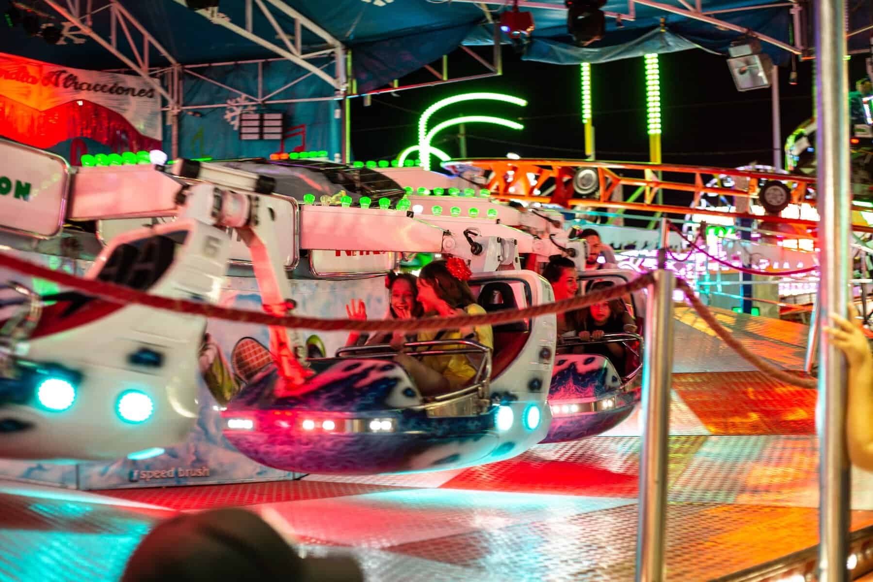 Atracción de feria en León con luces de neón y niños disfrutando en las naves espaciales.
