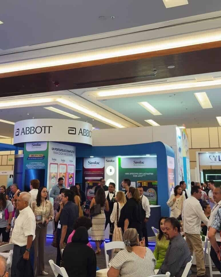Stand de Abbott en evento de salud con muchas personas interactuando y exhibiciones de productos médicos.