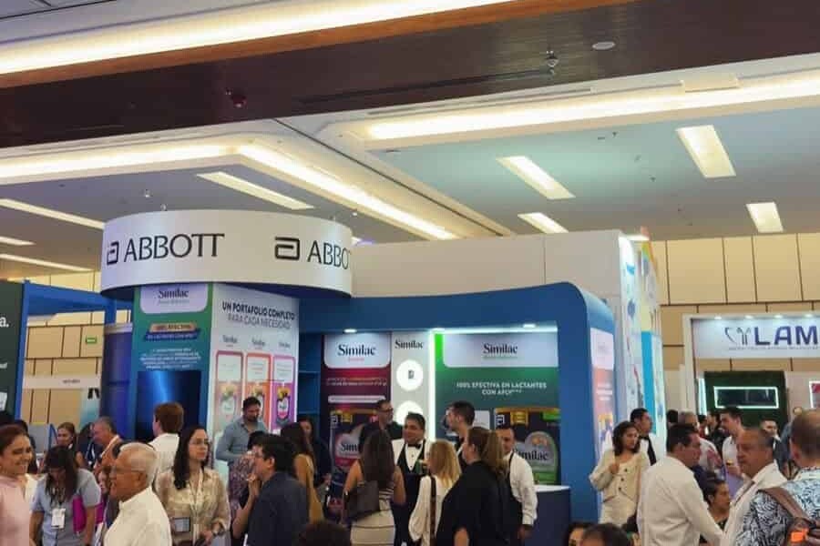 Stand de Abbott en evento de salud con muchas personas interactuando y exhibiciones de productos médicos.